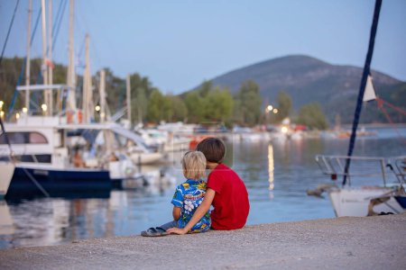 Téléchargez les photos : Enfant profitant d'une soirée incroyable dans la ville après le coucher du soleil, profitant des lumières et des bateaux sur une jetée - en image libre de droit