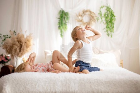 Téléchargez les photos : Enfants tout-petits doux mignons, pieds chatouillés sur le lit, riant et souriant, malice enfantin, bonheur - en image libre de droit
