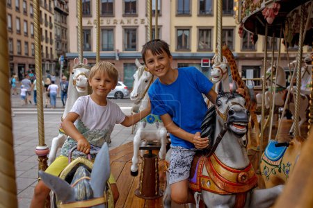 Photo for Children, boys, going on Merry Go Round, kids play on carousel summertime in Strasbourg, France during summer vacation - Royalty Free Image
