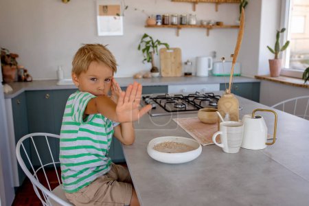 Photo for Beautiful blond child, boy, refusing to eat cereal for breakfast at home in the morning, sunny room - Royalty Free Image