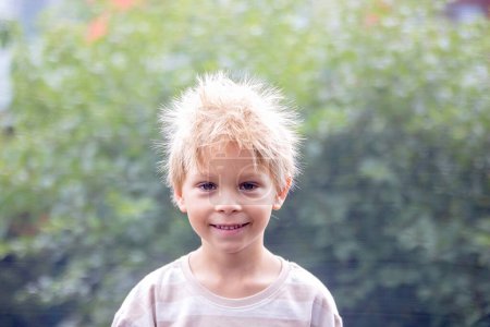 Foto de Lindo niño pequeño con pelo eléctrico estático, teniendo su retrato divertido tomado al aire libre en un trampolín - Imagen libre de derechos