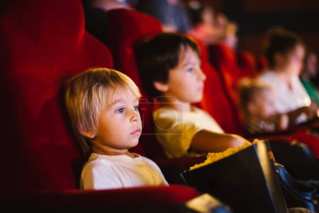 Photo for Cute child, boy, watching movie in a cinema, eating popcorn and enjoying the film - Royalty Free Image