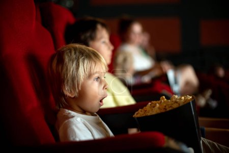 Téléchargez les photos : Cute child, boy, watching movie in a cinema, eating popcorn and enjoying the film - en image libre de droit