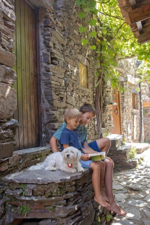 Téléchargez les photos : Beau village médiéval Talasnal à Lousa, Portugal par une belle journée. Enfant jouant dans la rue du village avec son chien de compagnie, livre de lecture - en image libre de droit