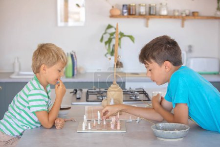 Foto de Chicos, hermanos, jugando ajedrez en casa, niños disfrutando de juegos de mesa juntos - Imagen libre de derechos