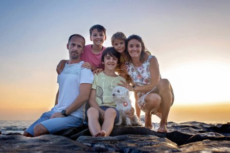 Foto de Niños felices, disfrutando de la puesta de sol sobre el océano con su familia, playa rocosa en Portugal - Imagen libre de derechos