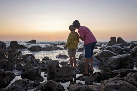Foto de Niños felices, disfrutando de la puesta de sol sobre el océano con su familia, playa rocosa en Portugal - Imagen libre de derechos