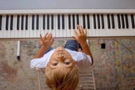 Photo for Child, blond boy, playing piano at home, learning - Royalty Free Image