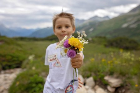 Téléchargez les photos : Belle enfant blonde, garçon, cueillette de fleurs sauvages de mère dans les montagnes en Suisse, été - en image libre de droit