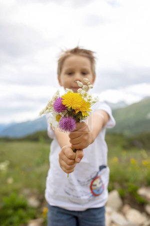 Foto de Hermoso niño rubio, niño, la recolección de flores silvestres fom madre en las montañas en Suiza, verano - Imagen libre de derechos