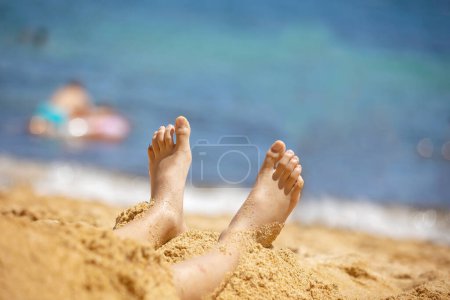 Photo for Child, tickling sibling on the beach on the feet with feather, kid cover in sand, smiling, laughing, enjoying some fun - Royalty Free Image