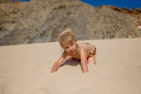 Foto de Niños felices, niños, jugando en la playa al atardecer, niños cubiertos de arena, sonriendo, riendo, disfrutando un poco de diversión - Imagen libre de derechos