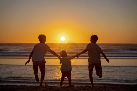 Téléchargez les photos : Enfants heureux, garçons, jouant sur la plage au coucher du soleil, enfant couvert de sable, souriant, riant, appréciant un peu de plaisir - en image libre de droit
