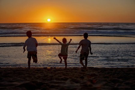 Foto de Niños felices, niños, jugando en la playa al atardecer, niños cubiertos de arena, sonriendo, riendo, disfrutando un poco de diversión - Imagen libre de derechos
