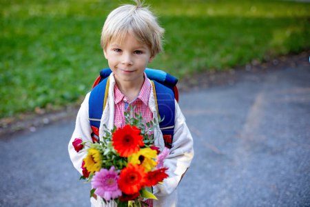 Téléchargez les photos : Premier jour à l'école pour un élève de première année, l'enfant commence l'école, apporter des fleurs pour l'enseignant, les membres de la famille vont avec lui - en image libre de droit