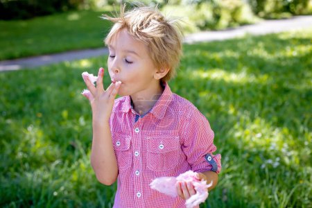 Foto de Lindo niño preescolar, comer algodón de azúcar rosa en el parque, verano - Imagen libre de derechos