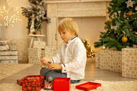 Foto de Lindo niño, niño, jugando en una habitación decorada para Navidad, lugar acogedor - Imagen libre de derechos