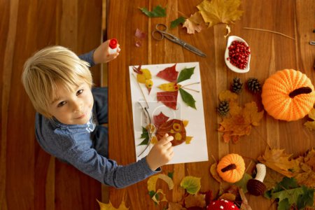 Téléchargez les photos : Enfant, appliquer des feuilles à l'aide de colle, ciseaux et peinture, tout en faisant de l'art et de l'artisanat à la maison ou à l'école - en image libre de droit