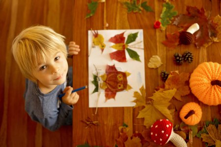 Photo for Child, applying leaves using glue, scissors, and paint, while doing arts and crafts at home or at school - Royalty Free Image