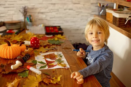 Photo for Child, applying leaves using glue, scissors, and paint, while doing arts and crafts at home or at school - Royalty Free Image