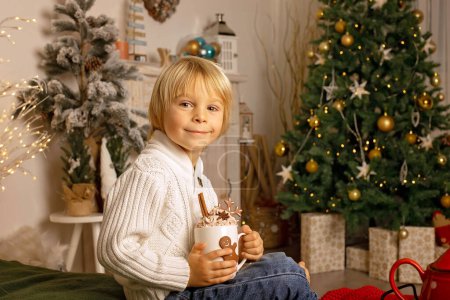 Foto de Lindo niño, niño, sentado en un sillón amarillo en una habitación decorada para Navidad, lugar acogedor - Imagen libre de derechos