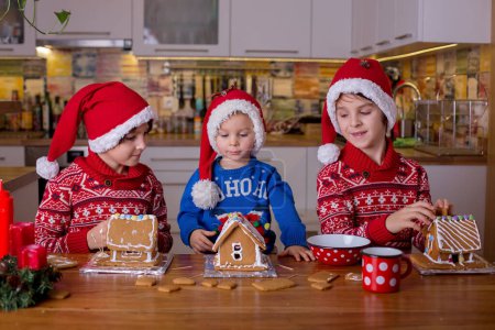 Téléchargez les photos : Enfants, garçons, décoration de maisons de pain au gingembre faites maison à la maison avec maman les aider - en image libre de droit