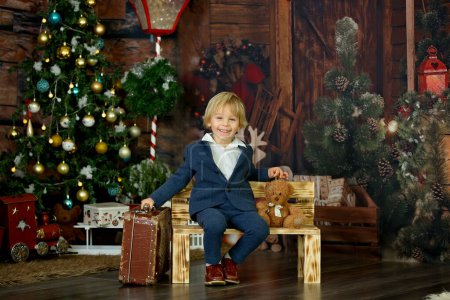 Photo for Cute child, holding suitcase and teddy bear, waiting at home for holidays, studio shot - Royalty Free Image