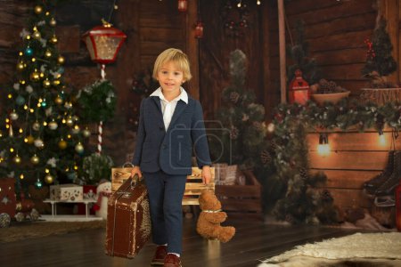 Photo for Cute child, holding suitcase and teddy bear, waiting at home for holidays, studio shot - Royalty Free Image
