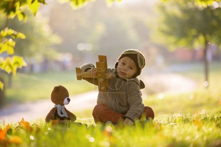 Foto de Niño pequeño, niño, jugando con el avión y el oso de peluche de punto en el parque de otoño al atardecer - Imagen libre de derechos