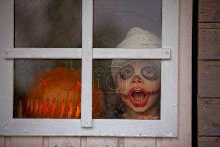 Foto de Niño asustadizo en traje de halloween, jugando con calabazas talladas y velas - Imagen libre de derechos