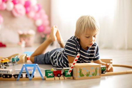 Téléchargez les photos : Cute child, blond toddler boy, playing with wooden trains at home - en image libre de droit