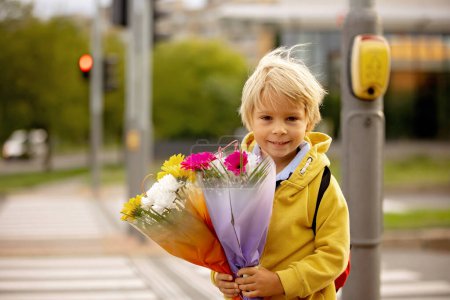 Photo for Cute preschool child, waiting on a red light to cross the street, caring bouquets of flowers for teachers, going to preschool, first day at school - Royalty Free Image