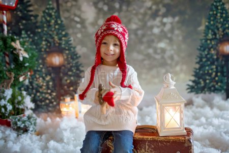 Téléchargez les photos : Enfant tout-petit Littlw avec valise et petit jouet gingembre à la main, marchant dans une forêt enneigée, photo de thème de Noël - en image libre de droit