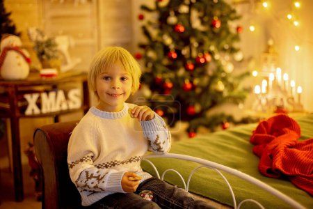 Foto de Lindo niño, niño, sentado en un sillón amarillo en una habitación decorada para Navidad, lugar acogedor - Imagen libre de derechos