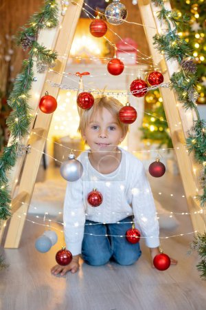 Photo for Beautiful blond child, young school boy, playing in a decorated home with knitted toys at Christmas - Royalty Free Image