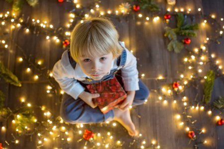 Téléchargez les photos : Enfant en bas âge, mignon garçon blond, assis sur le sol avec chien de compagnie, lumières de Noël autour de lui - en image libre de droit