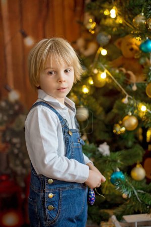 Foto de Toddler child, cute blond boy, decorating christmas tree, christmas lights around him - Imagen libre de derechos