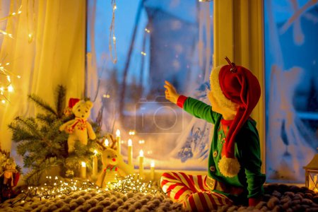 Photo for Cute toddler child in pajama, sitting on a fury blanket next to a window, looking outside at fireworks on New Years Eve - Royalty Free Image