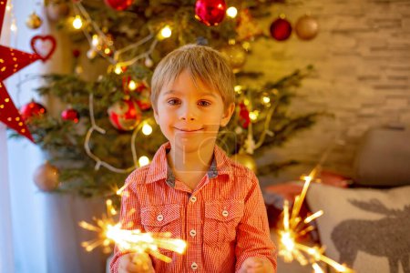 Foto de Child holding sparkler at home at New Years Eve, enjoying happy evening with family - Imagen libre de derechos