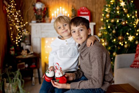 Photo for Beautiful blond child and his old brother, young school boys, playing in a decorated home with knitted toys at Christmas, eating cookies and drinking milk - Royalty Free Image