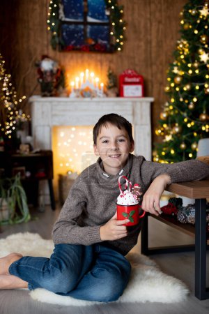 Foto de Hermoso niño rubio y su hermano mayor, niños de la escuela, jugando en una casa decorada con juguetes de punto en Navidad, comiendo galletas y bebiendo leche - Imagen libre de derechos
