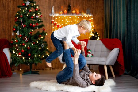 Schönes blondes Kind, kleiner Schuljunge, der zu Weihnachten in einem geschmückten Haus mit Strickspielzeug spielt