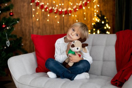 Foto de Hermoso niño rubio, niño de la escuela, jugando en una casa decorada con juguetes de punto en Navidad - Imagen libre de derechos