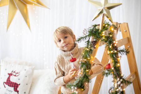 Foto de Hermoso niño rubio, niño de la escuela, jugando en una casa decorada con juguetes de punto en Navidad - Imagen libre de derechos
