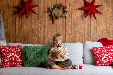 Photo for Beautiful blond child, young school boy, playing in a decorated home with knitted toys at Christmas - Royalty Free Image