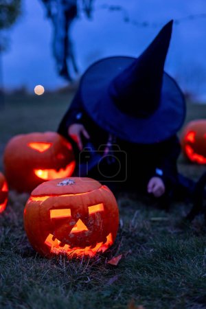 Photo for Two boys in the park with Halloween costumes, carved pumpkins with candles and decoration, playing - Royalty Free Image