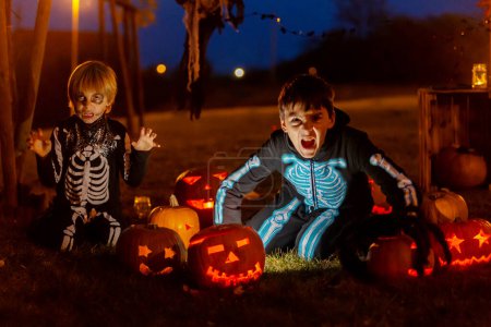Foto de Dos chicos en el parque con disfraces de Halloween, calabazas talladas con velas y decoración, jugando - Imagen libre de derechos