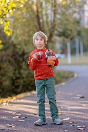 Photo for Beautiful blond preschool child, boy, sitting in the park in the morning sunrise, enjoying autumn weather, drinking tea and enjoying the sun - Royalty Free Image