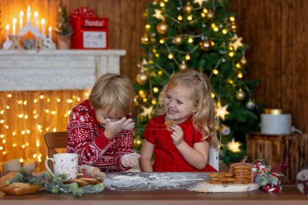 Foto de Hermosos niños, niños rubios, hermanos, jugando en casa decorada para Navidad, disfrutando de vacaciones en casa - Imagen libre de derechos
