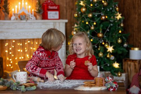 Foto de Hermosos niños, niños rubios, hermanos, jugando en casa decorada para Navidad, disfrutando de vacaciones en casa - Imagen libre de derechos